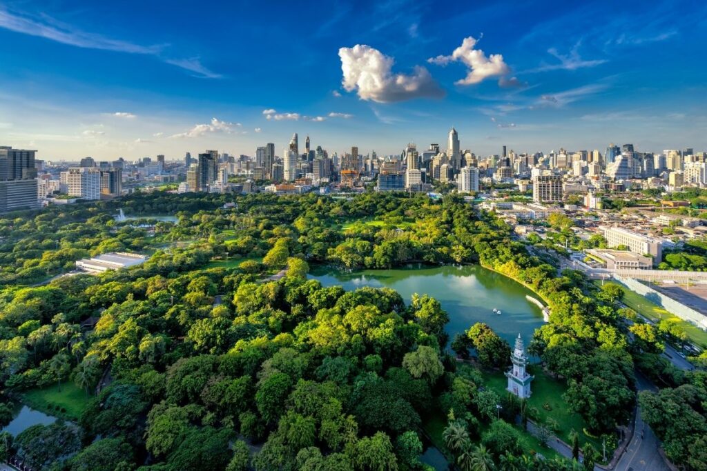Aerial view of green trees and lake in Benjakitti Forest Park with Bangkok skyline